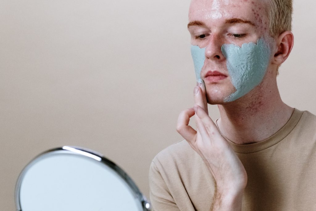 Man with clogged pores is putting cream on face.
