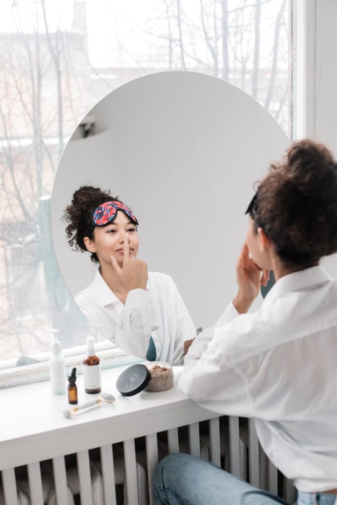 Woman touching her nose while looking at herself in the mirror
